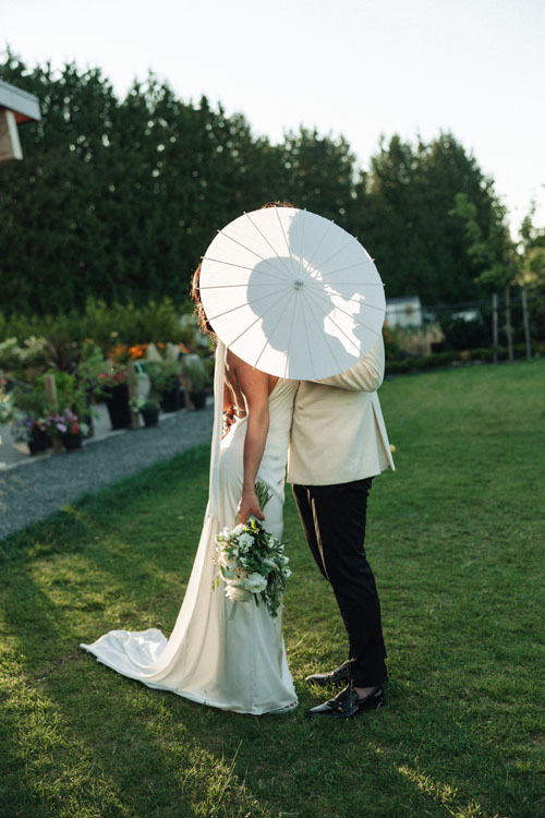Bride and groom kissing behind a white parasol on the lawn