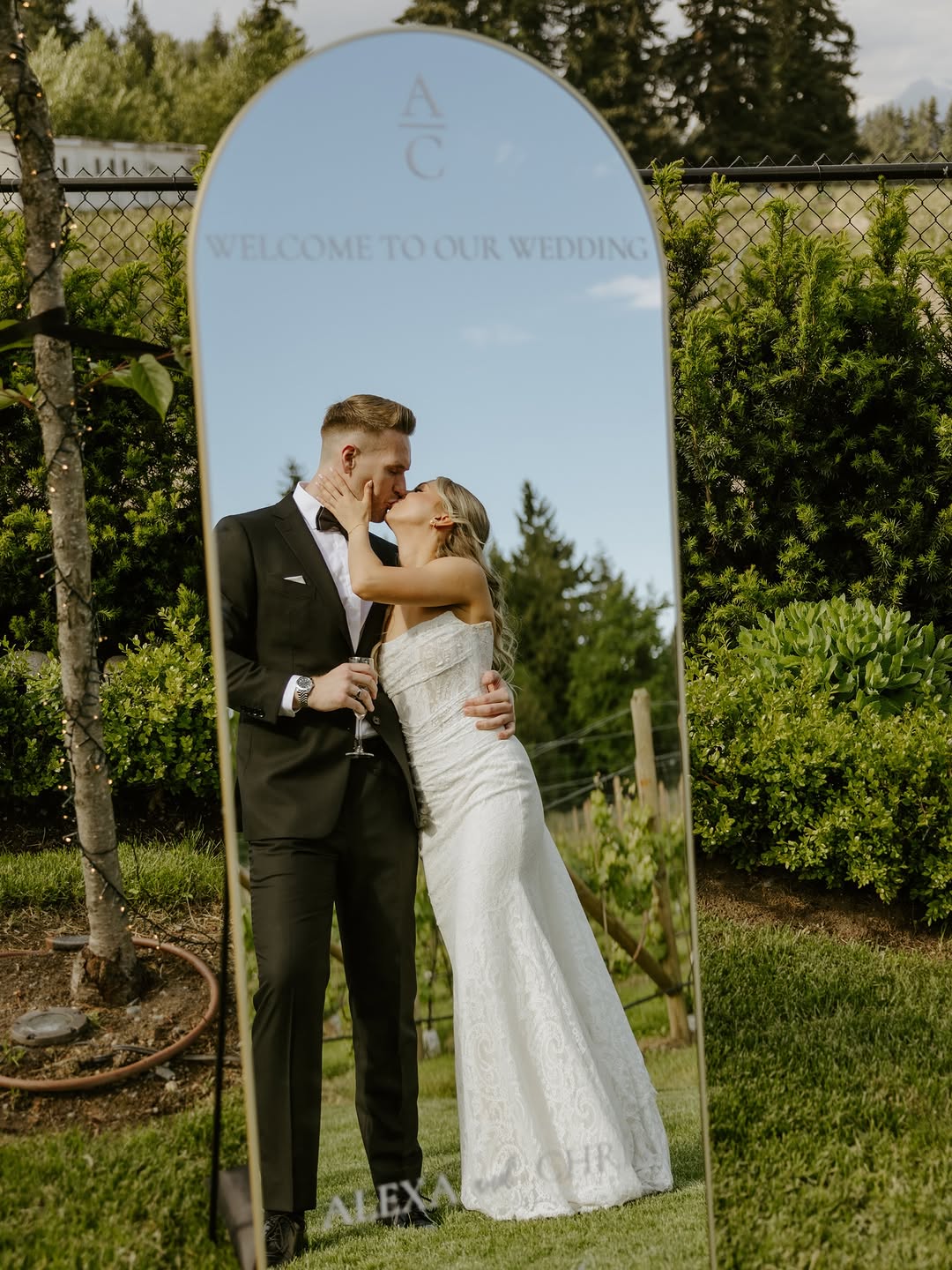 Bride and groom kissing reflected in an arched welcome mirror